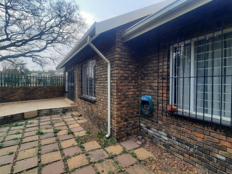 Rear exterior view of the townhouse featuring a face brick facade, security bars on windows, and a paved patio area with boundary walling.