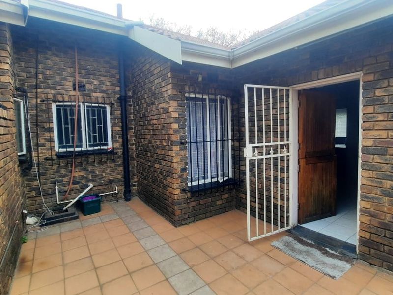 Rear exterior view of the townhouse featuring a tiled patio area, face brick facade, and secure access via a timber door with a security gate.