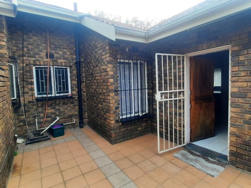 A rear exterior view of the townhouse featuring a tiled patio area, face brick walls, and secure access via a timber door with security gate.
