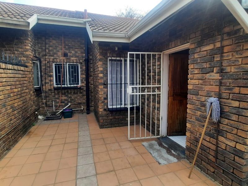 A rear exterior view of a face brick townhouse featuring a tiled patio area, security gates, and security bars on the windows.