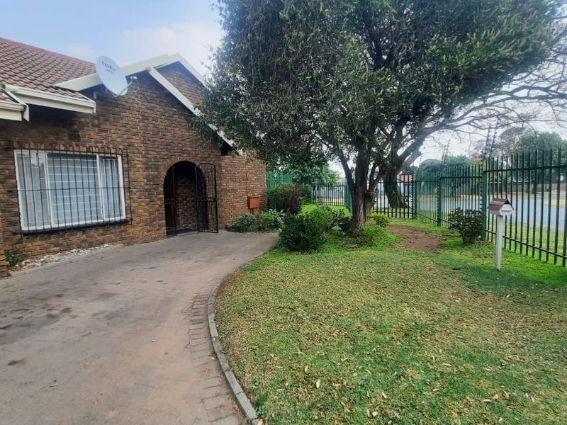 Front exterior view of a face brick townhouse featuring a paved driveway, security fencing, and established garden area.