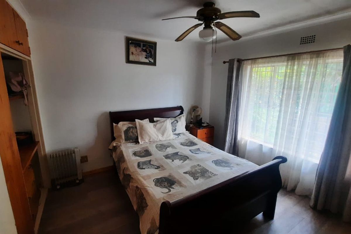 A functional bedroom featuring laminate flooring, a ceiling fan, and a built-in wardrobe with window security bars for added safety.