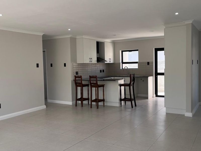 Modern open-plan living area featuring a sleek kitchen with built-in cabinetry, a central island, and neutral tiled flooring throughout.