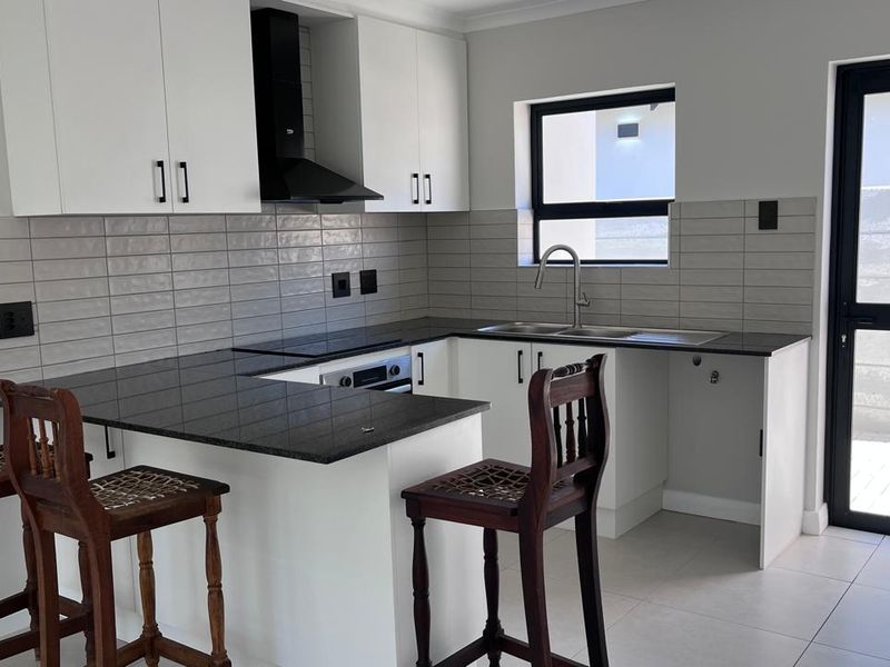 Modern kitchen featuring white cabinetry, dark granite countertops, integrated appliances, tiled backsplash, and direct access to the exterior.