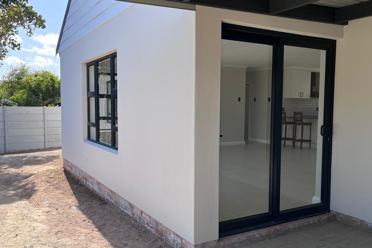 Rear exterior view showing a paved patio area, modern sliding glass doors, and aluminium window frames with a clean rendered finish.