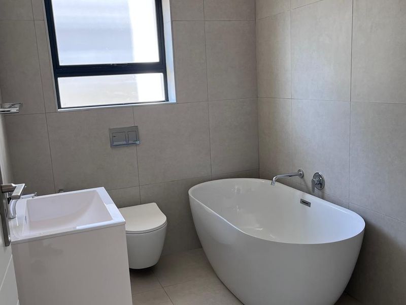 Modern bathroom featuring a sleek freestanding bathtub, wall-mounted toilet, and contemporary vanity basin with neutral floor-to-ceiling tiling.