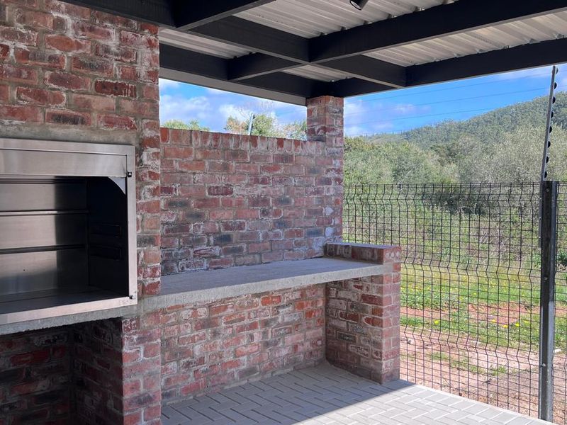 Covered outdoor patio featuring a built-in stainless steel braai, brick masonry construction, concrete prep surface, and paved flooring with scenic views.