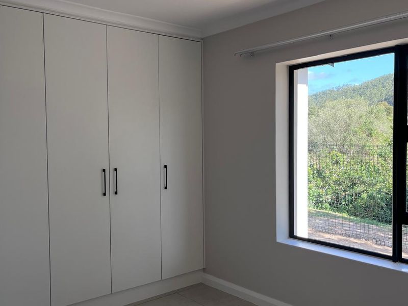 A bright, empty bedroom featuring modern built-in cupboards and a large window with scenic views.
