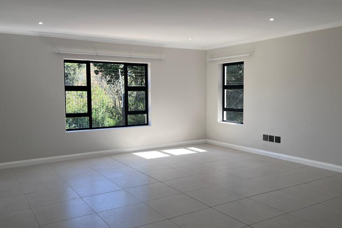 A bright, spacious, and empty living area featuring neutral tiled flooring, modern black aluminium windows, and recessed downlighting.