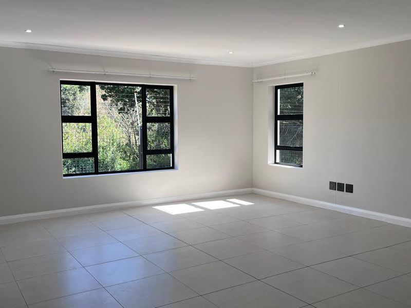 A bright, spacious, and empty living area featuring neutral tiled flooring, modern black aluminium windows, and recessed downlighting.