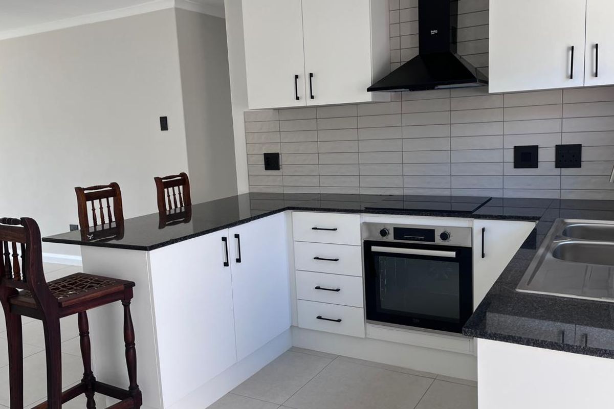 Modern kitchen featuring white cabinetry, granite countertops, a built-in oven with hob, extractor fan, and a tiled backsplash.