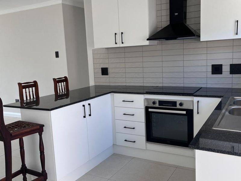 Modern kitchen featuring white cabinetry, granite countertops, a built-in oven with hob, extractor fan, and a tiled backsplash.
