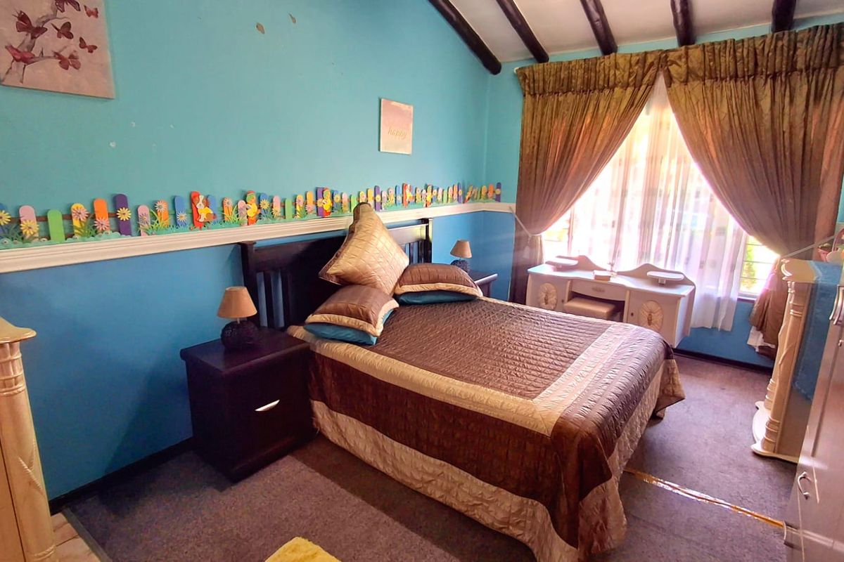 A bedroom featuring exposed timber ceiling beams, blue painted walls, and carpeted flooring, providing a functional sleeping space.
