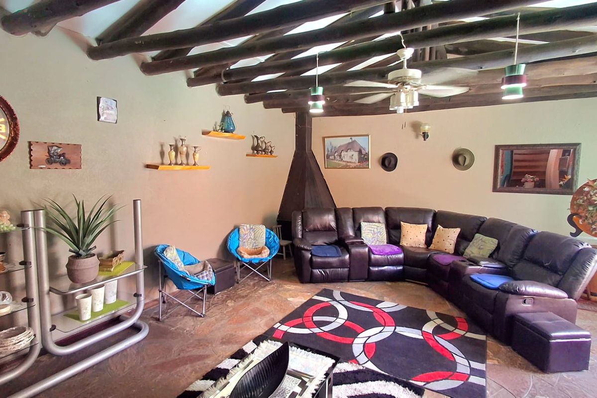 A rustic living room featuring exposed timber ceiling beams, a built-in corner fireplace, and natural stone flooring.