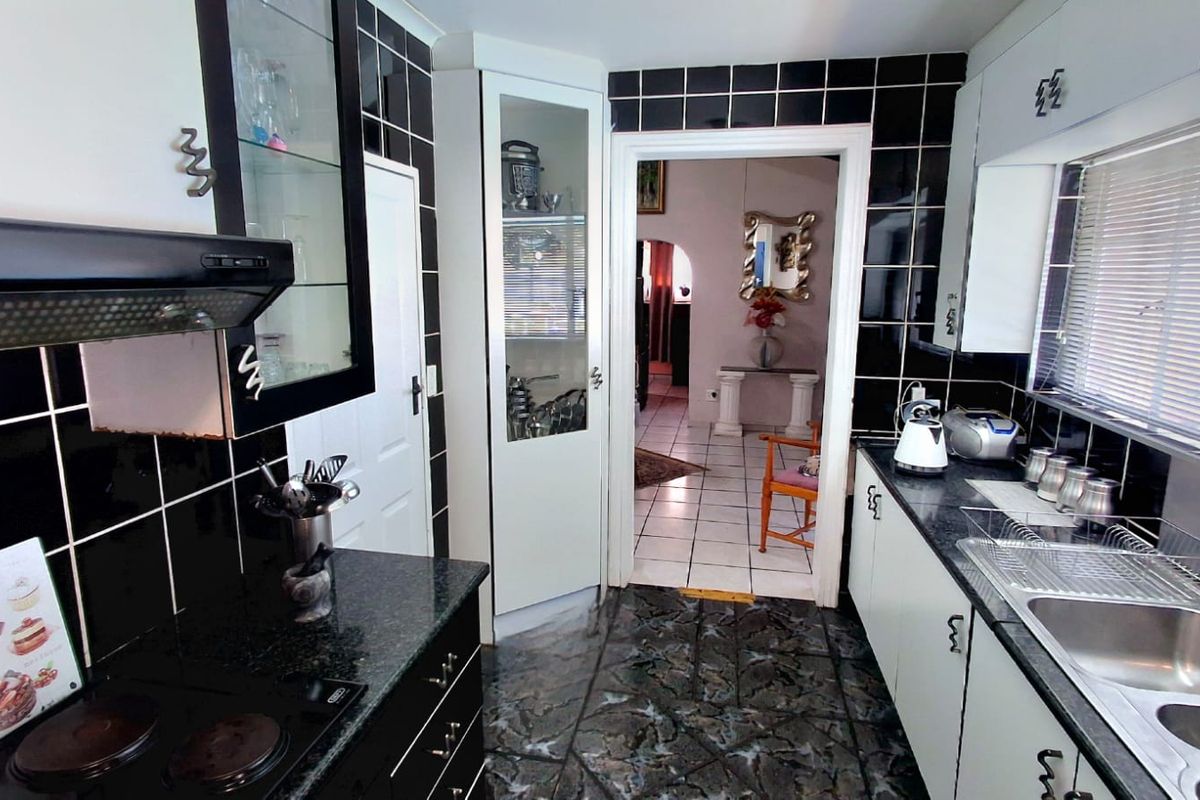 A functional kitchen featuring black granite-style countertops, white cabinetry, a built-in extractor fan, and high-contrast black wall tiles.