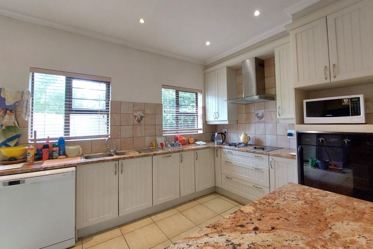 A functional kitchen featuring granite countertops, built-in oven, stainless steel extractor fan, and ample cabinetry with tiled backsplash and flooring.