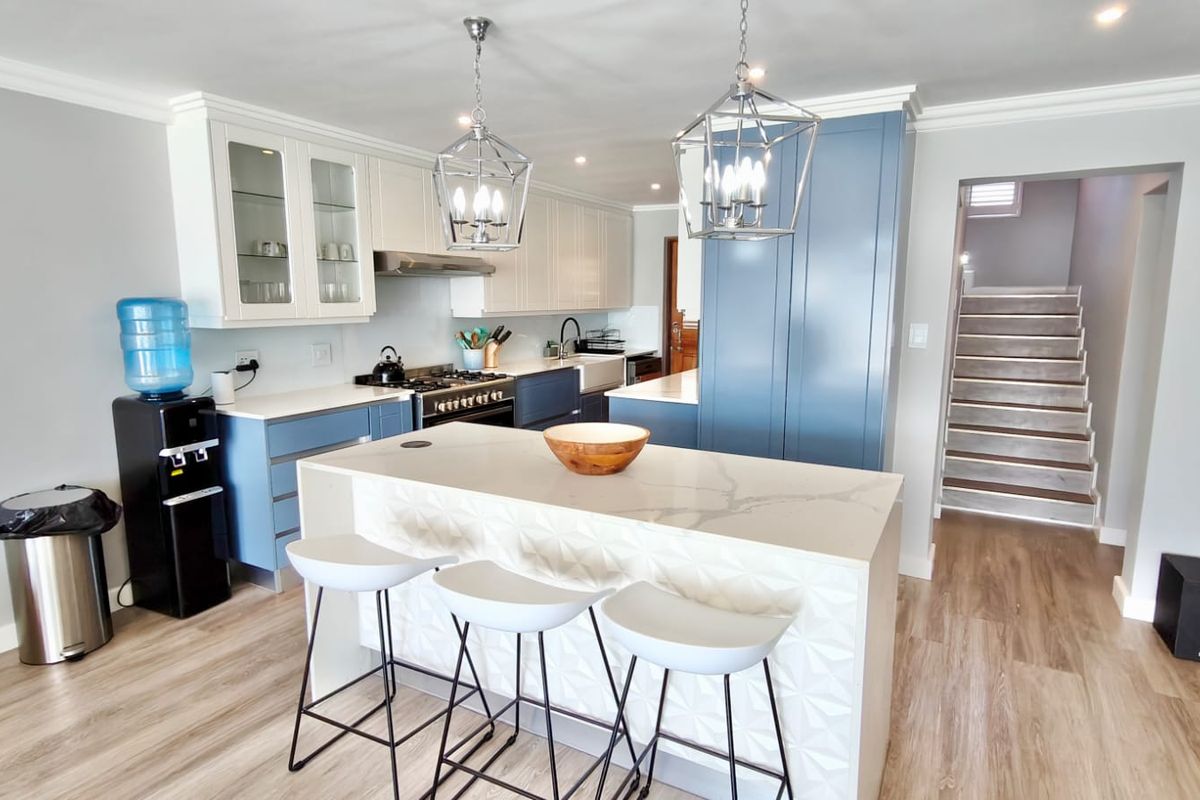 Modern kitchen featuring a central island with quartz countertops, blue and white cabinetry, gas range, and stylish pendant lighting, leading to a staircase.