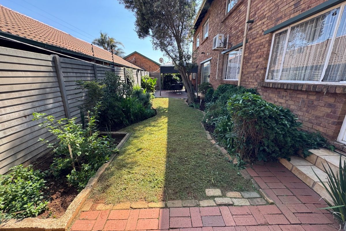A private rear garden featuring a brick-paved walkway, established garden beds, and a lawn area adjacent to the townhouse exterior.