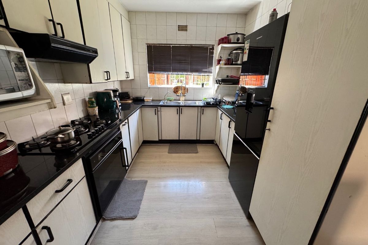 A functional U-shaped kitchen featuring black countertops, white cabinetry, a built-in oven, gas hob, and an extractor fan.