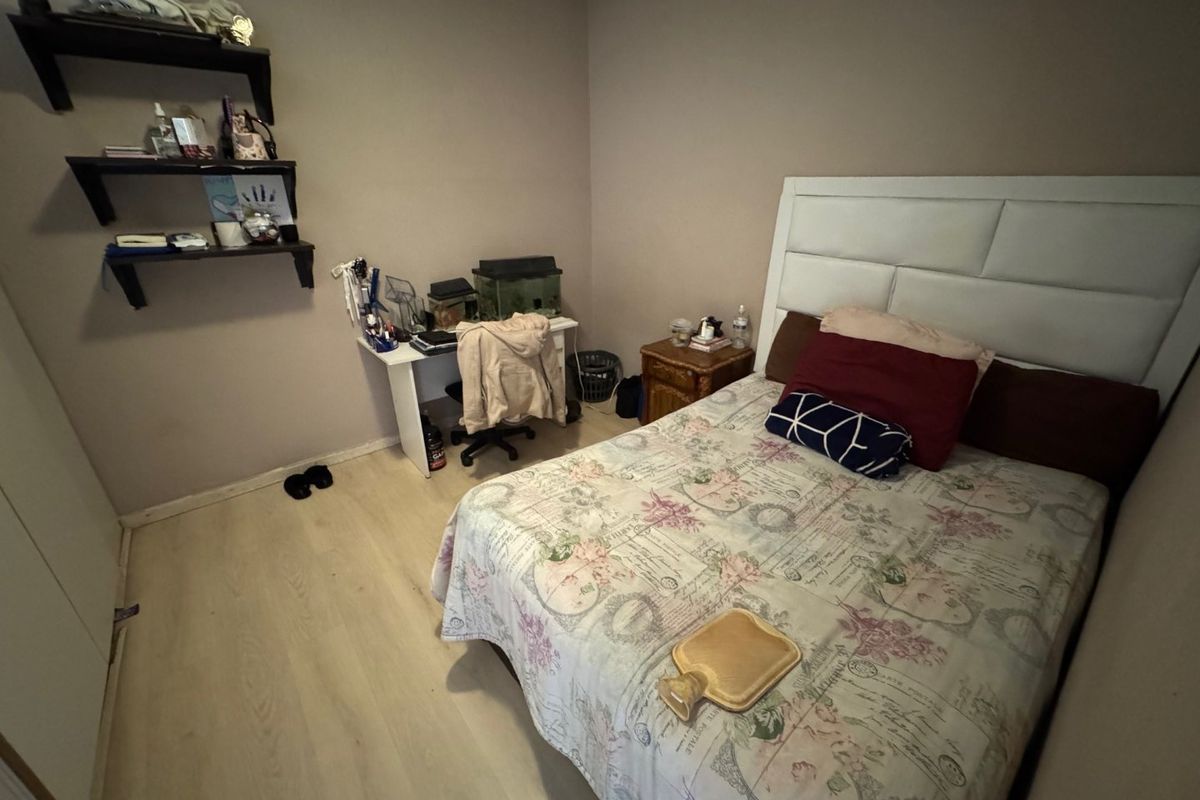 A standard bedroom featuring light-toned laminate flooring and built-in wall shelving.