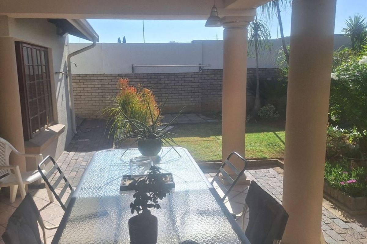 A covered patio area featuring structural columns, tiled flooring, and direct access to a private garden with brick boundary walls.