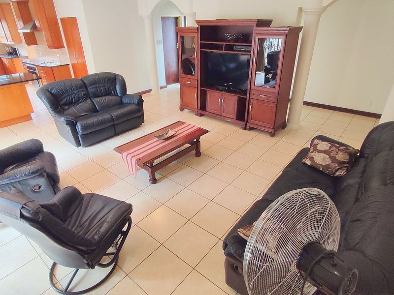 Spacious open-plan living area featuring tiled floors, integrated kitchen cabinetry with granite countertops, and architectural columns connecting to the kitchen space.