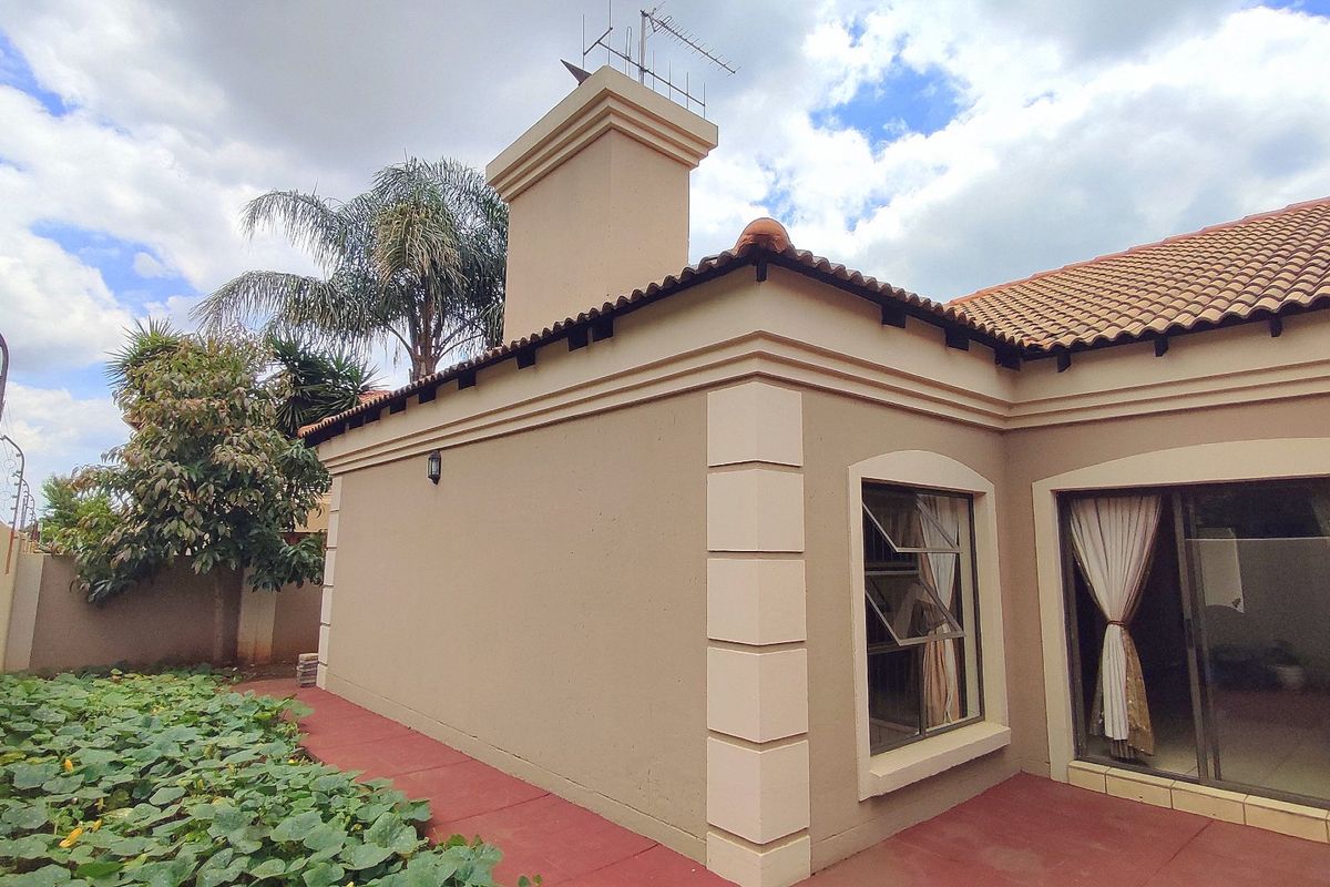 Rear exterior view of the property featuring a chimney, tiled roof, and sliding glass doors leading to a paved patio area.