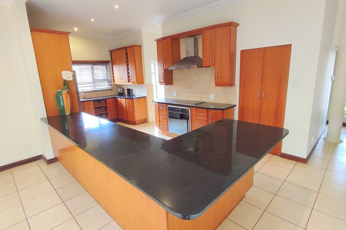 A spacious kitchen featuring granite countertops, built-in cabinetry, an integrated oven and hob, and tiled flooring throughout.