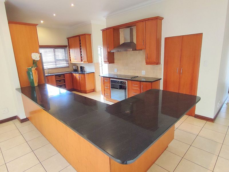 A spacious kitchen featuring granite countertops, built-in cabinetry, an integrated oven and hob, and tiled flooring throughout.