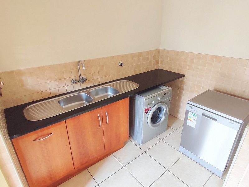 A functional laundry area featuring a double bowl stainless steel sink, laminate countertop, wooden cabinetry, and tiled backsplash.