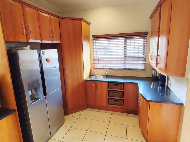 A functional kitchen featuring warm-toned wooden cabinetry, dark granite countertops, tiled flooring, and a window with fitted venetian blinds.