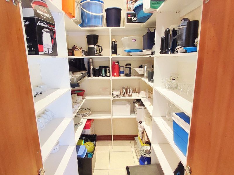 A functional walk-in pantry or scullery featuring extensive built-in shelving for organized storage and durable tiled flooring.
