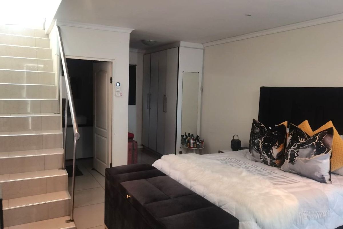 A bedroom featuring tiled flooring, built-in cupboards, and an internal staircase with a stainless steel handrail leading to an upper level.
