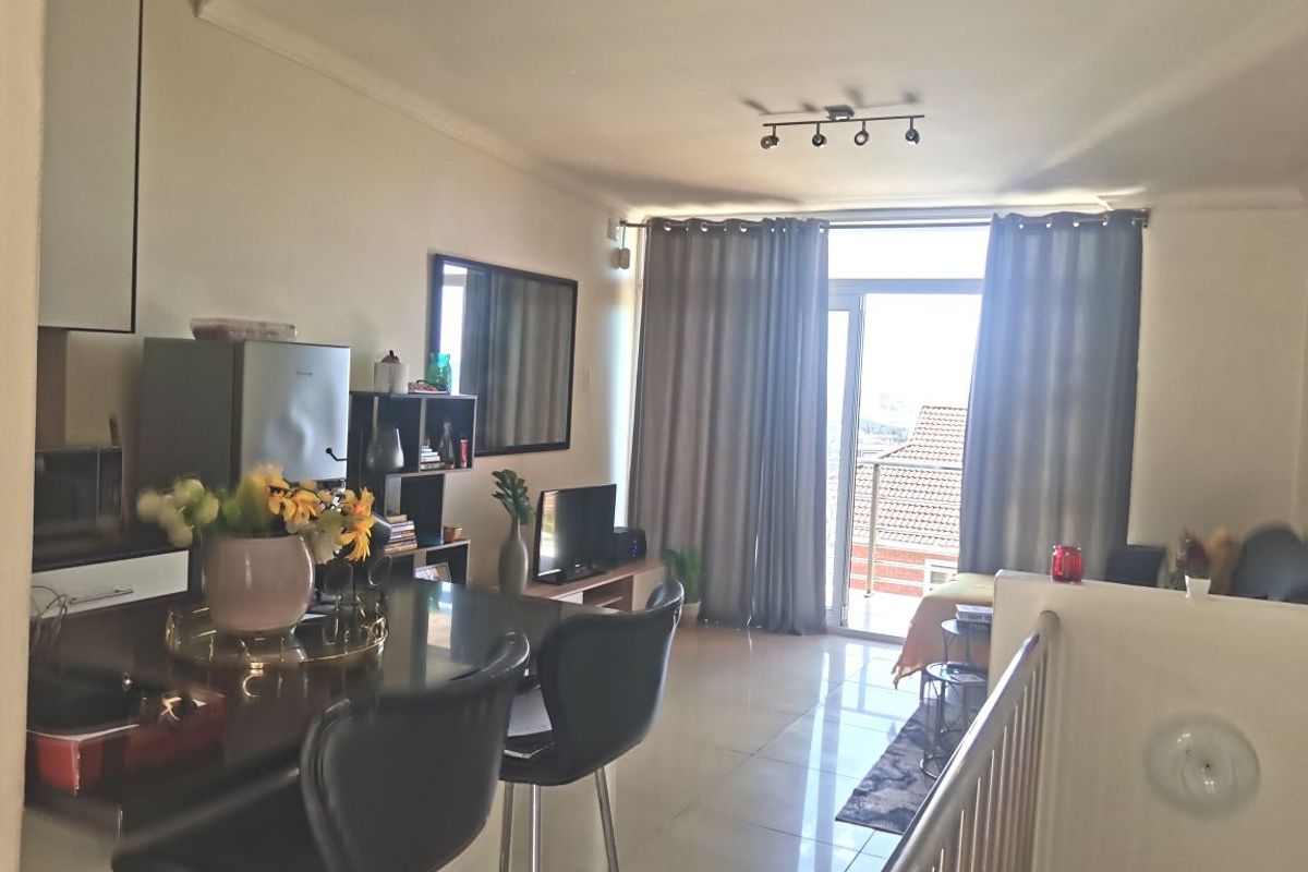Open-plan living area featuring tiled flooring, track lighting, and a sliding glass door leading to a balcony, providing natural light and access.