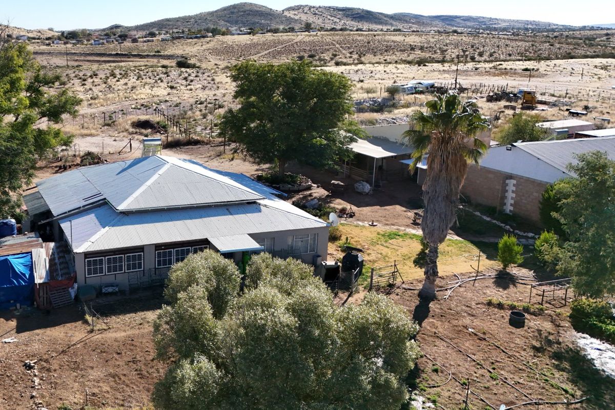 Aerial view of a farm property featuring a main dwelling with a corrugated metal roof, surrounding outbuildings, and expansive dry landscape.