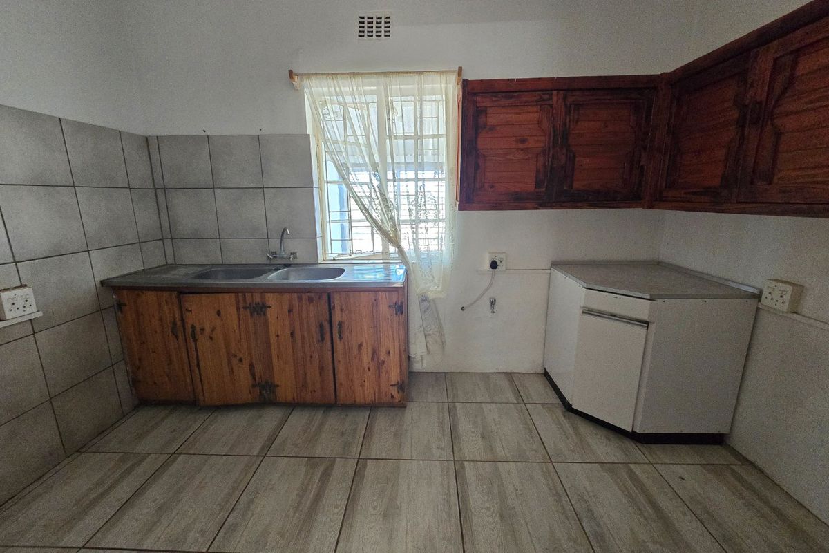 A functional kitchen space featuring tiled flooring, built-in wooden cabinetry, and a stainless steel sink, offering a blank canvas for modern renovation.