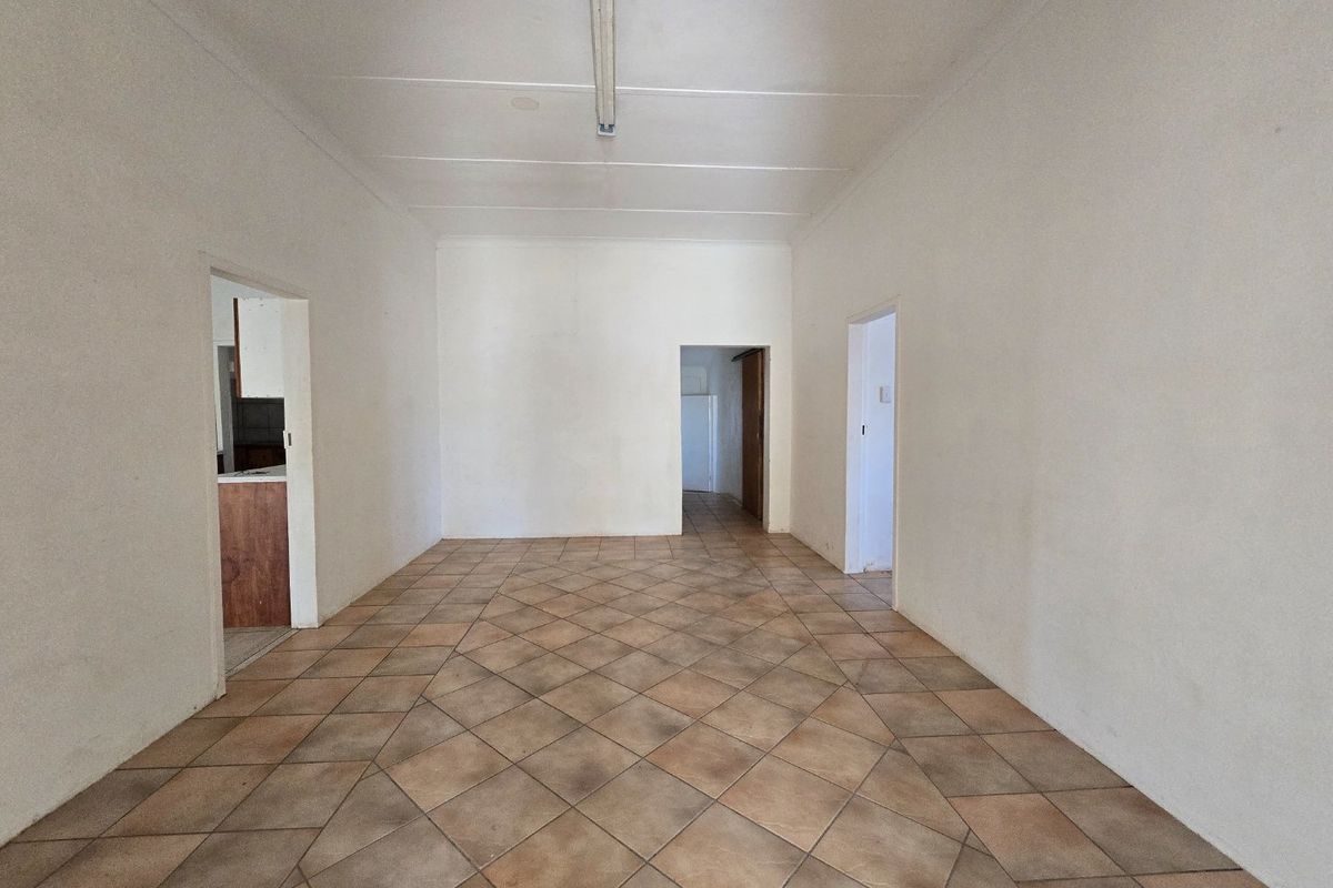 An empty, open-plan living area featuring neutral walls and diamond-patterned ceramic floor tiles, providing a blank canvas for renovation.