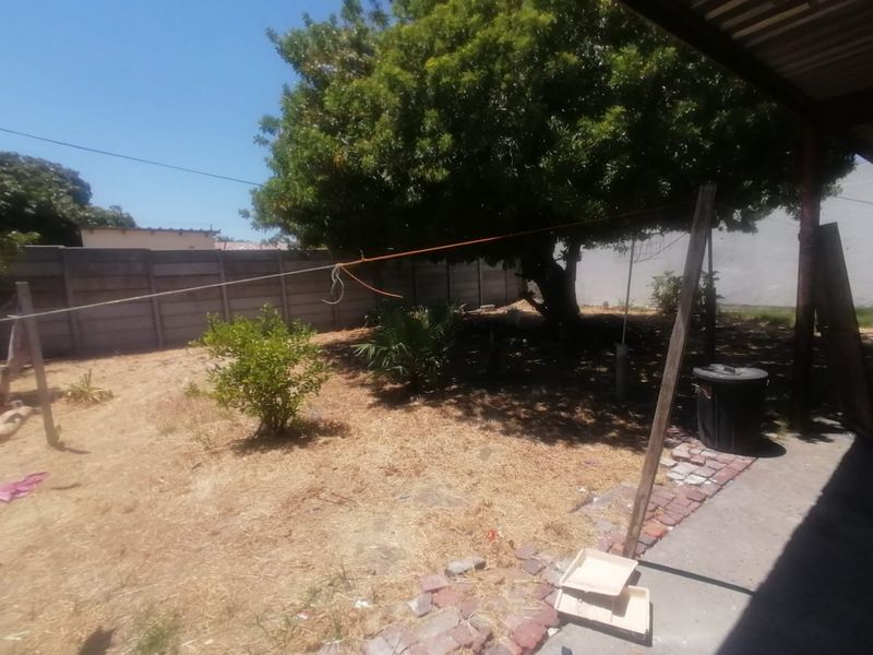 A rear garden area featuring a precast concrete boundary wall, brick paving, and established trees, requiring landscaping and maintenance.