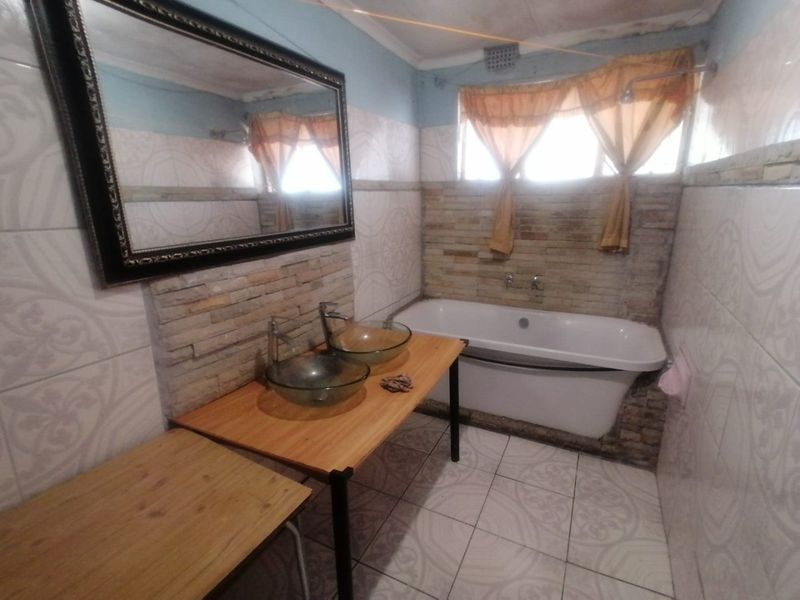 Bathroom featuring a freestanding bathtub, dual glass vessel sinks on a wooden vanity, and stone-clad feature walls.