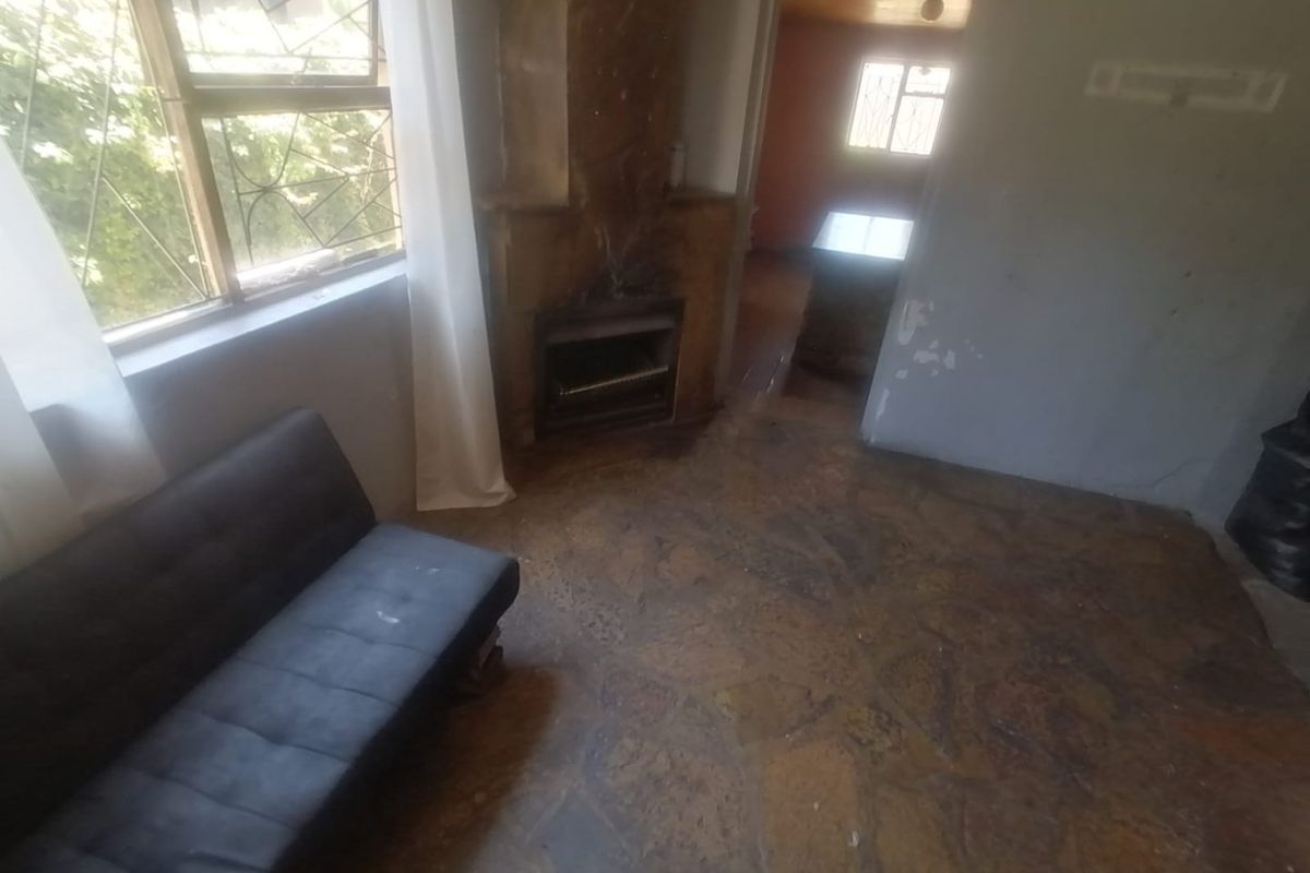 Living room featuring a stone fireplace and traditional flagstone flooring, with access to an adjacent room and natural light through large windows.