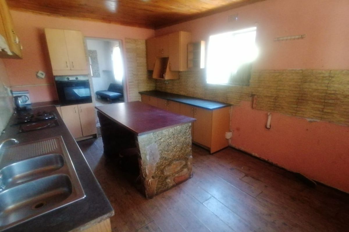 A dated kitchen featuring timber ceilings, laminate cabinetry, a central island, and built-in oven, requiring cosmetic updates and repairs to wall finishes.