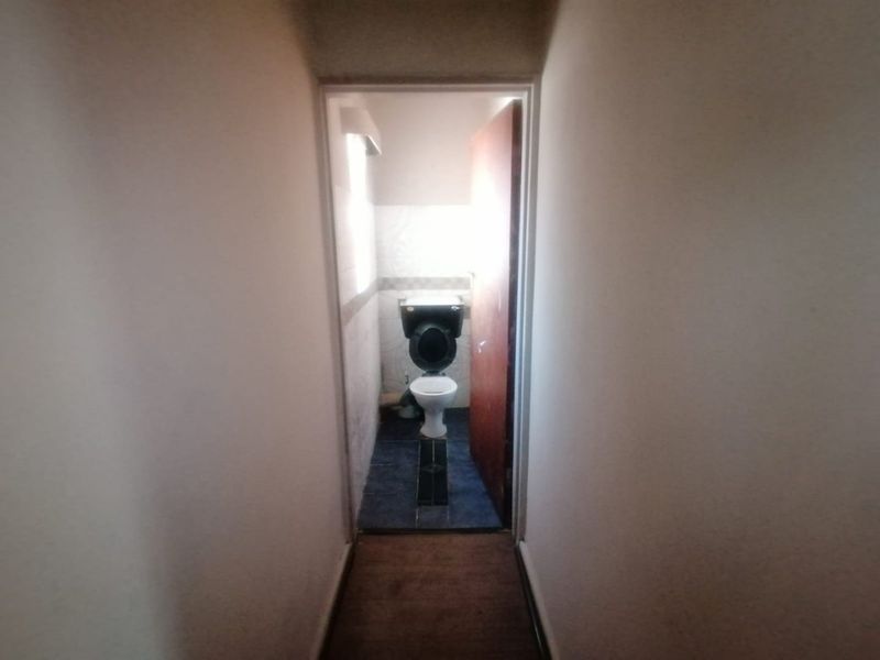A small, functional bathroom featuring a toilet and tiled flooring, currently in need of cosmetic updates to improve its overall condition and appeal.