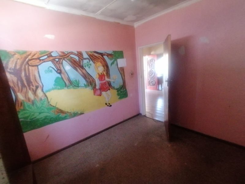 An empty bedroom featuring pink walls with a mural, carpet flooring, and a coved ceiling, requiring cosmetic updates to improve its overall condition.