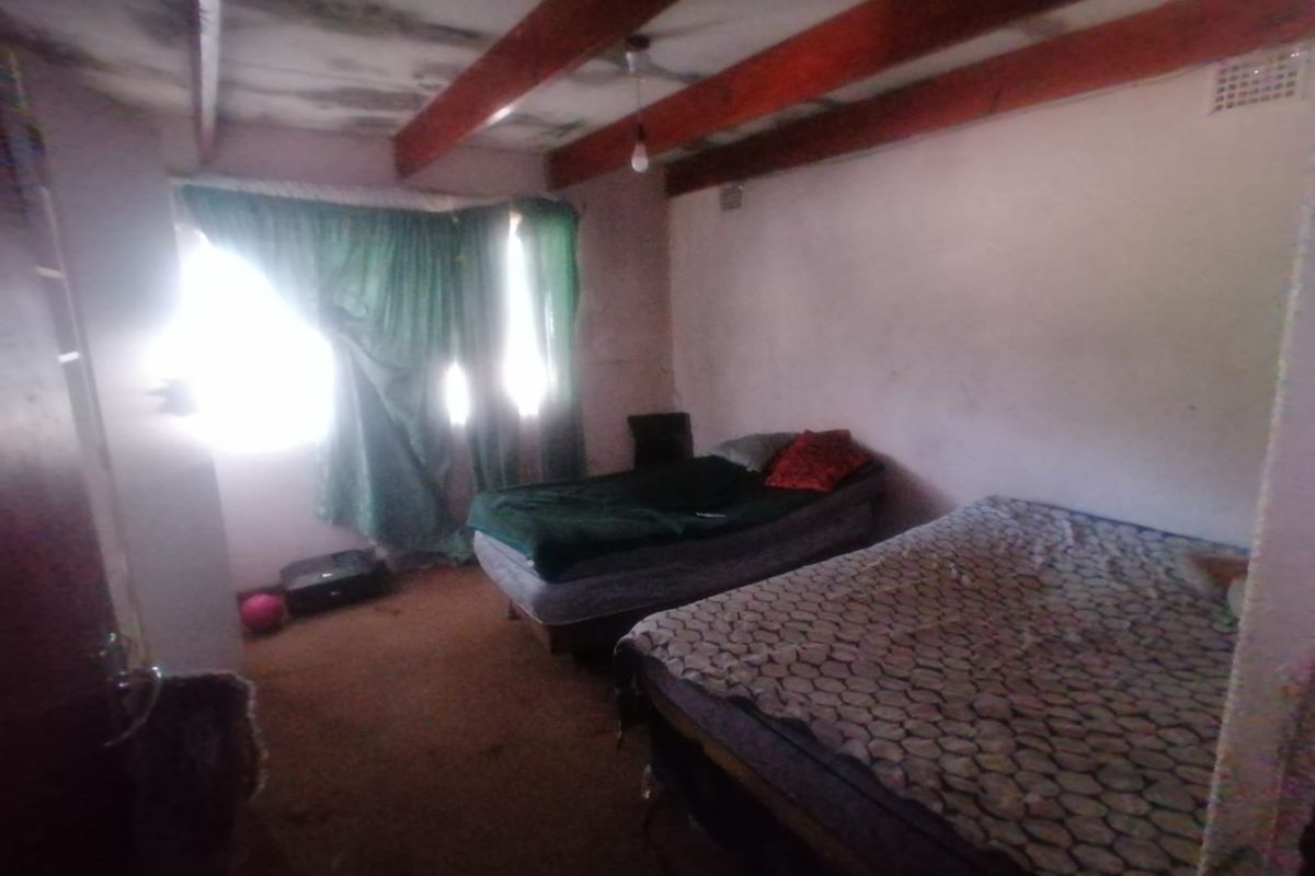 A bedroom featuring exposed timber ceiling beams and a ventilation grille, currently showing significant signs of wear and ceiling damage.