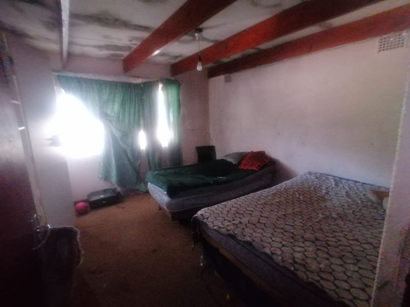 A bedroom featuring exposed timber ceiling beams and a ventilation grille, currently showing significant signs of wear and ceiling damage.