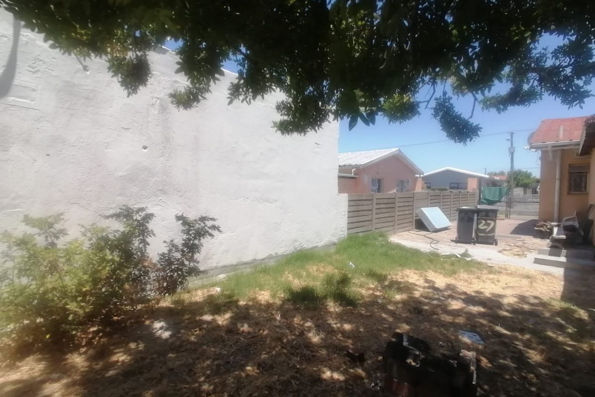 A view of the rear yard featuring a large plastered wall and precast concrete boundary fencing.