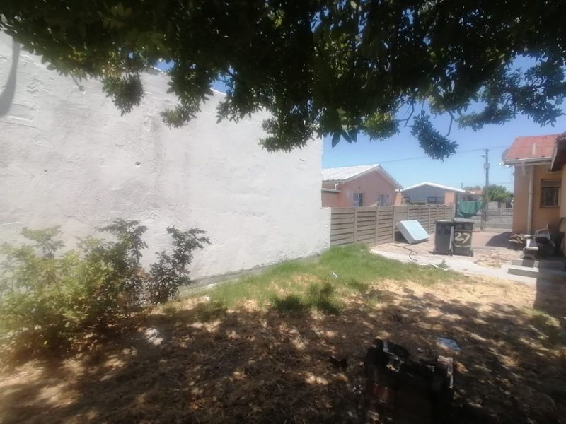 A view of the rear yard featuring a large plastered wall and precast concrete boundary fencing.