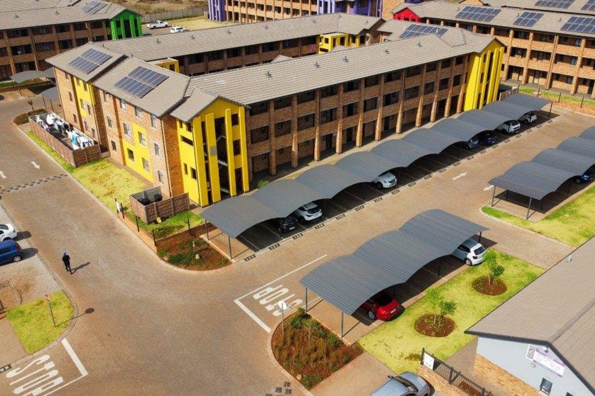 Aerial view of an apartment complex featuring brick buildings with tiled roofs, solar panels, and covered parking bays.