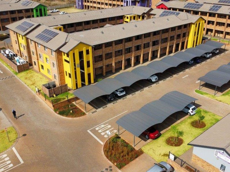 Aerial view of an apartment complex featuring brick buildings with tiled roofs, solar panels, and covered parking bays.