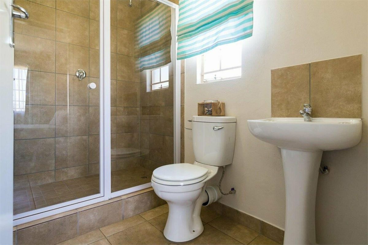 A functional bathroom featuring a pedestal basin, toilet, and a tiled shower enclosure with a glass door.